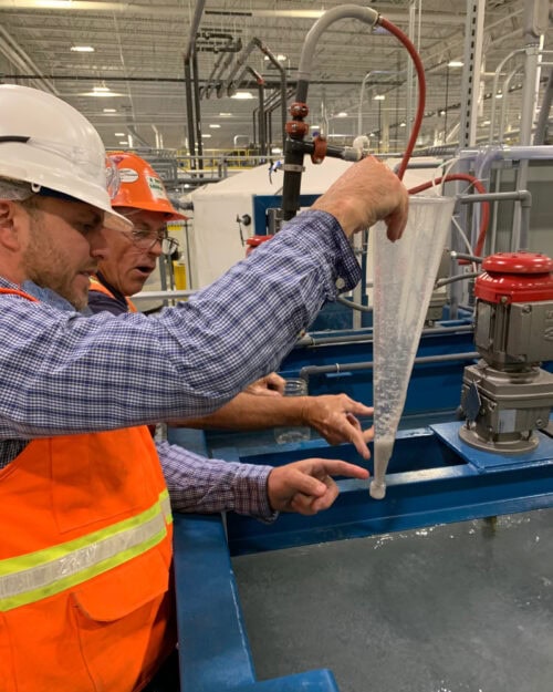 Two Anguil engineers performing scientific tests on a plastic beaker full of wastewater.